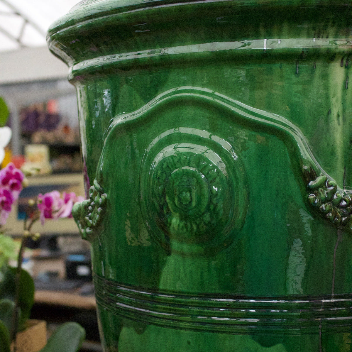 Close-up of a green decorative vase with intricate designs, blurred indoor background.