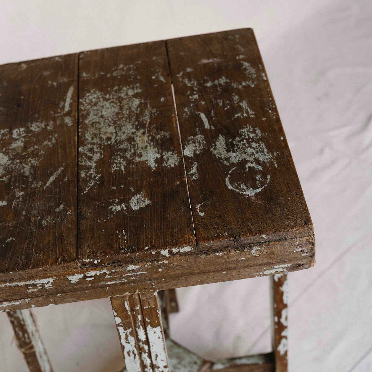 A rustic dark brown wooden table with a distressed finish, showing peeling white paint and weathered texture on the tabletop and legs, photographed against a light fabric background.