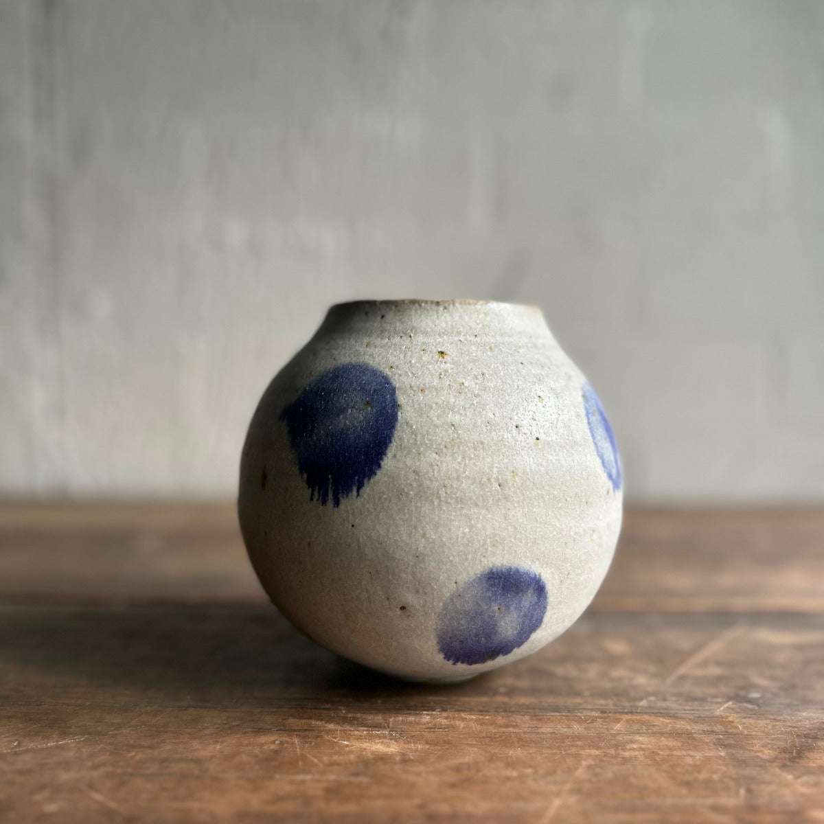 Ceramic vase with blue spots on a wooden surface and gray background