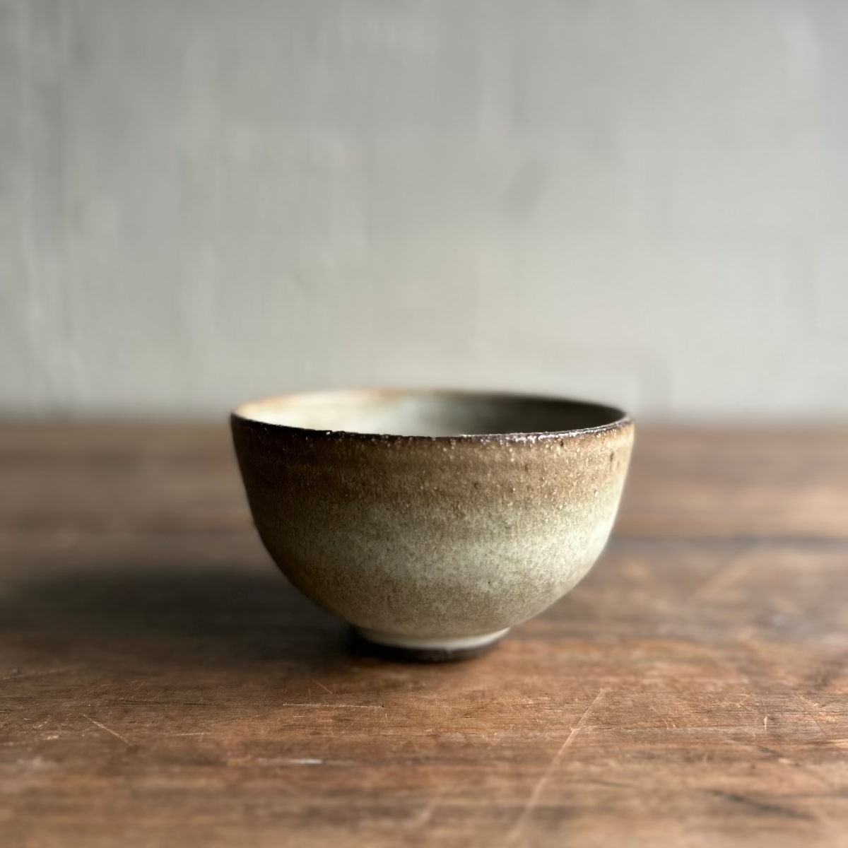 A handmade ceramic bowl with a textured, speckled glaze in earthy brown and beige tones, Japanese style.