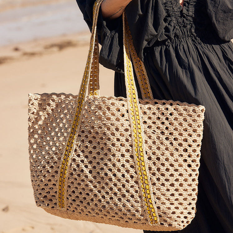 Person holding a woven handbag on a beach
