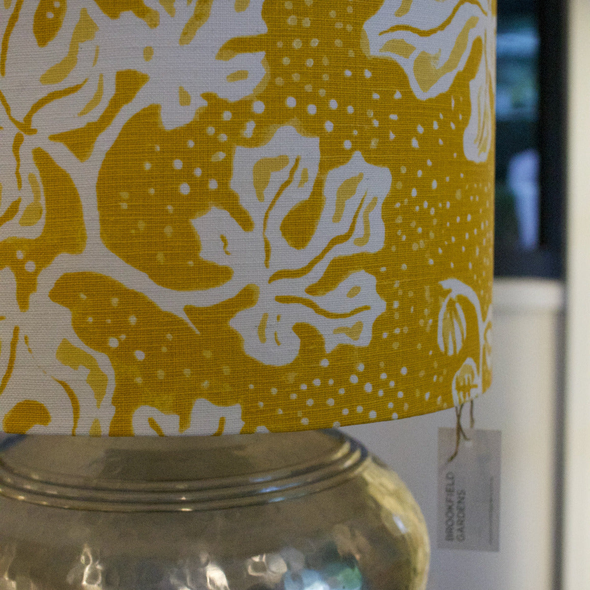 Yellow and white floral patterned lampshade on a glass jar with a blurred background.