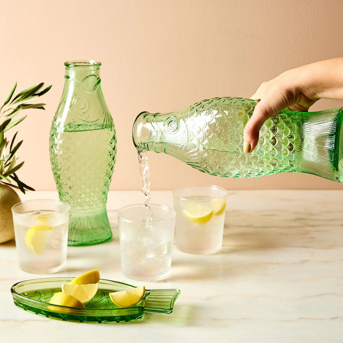 Person pouring lemonade from a green glass bottle into glasses on a table.