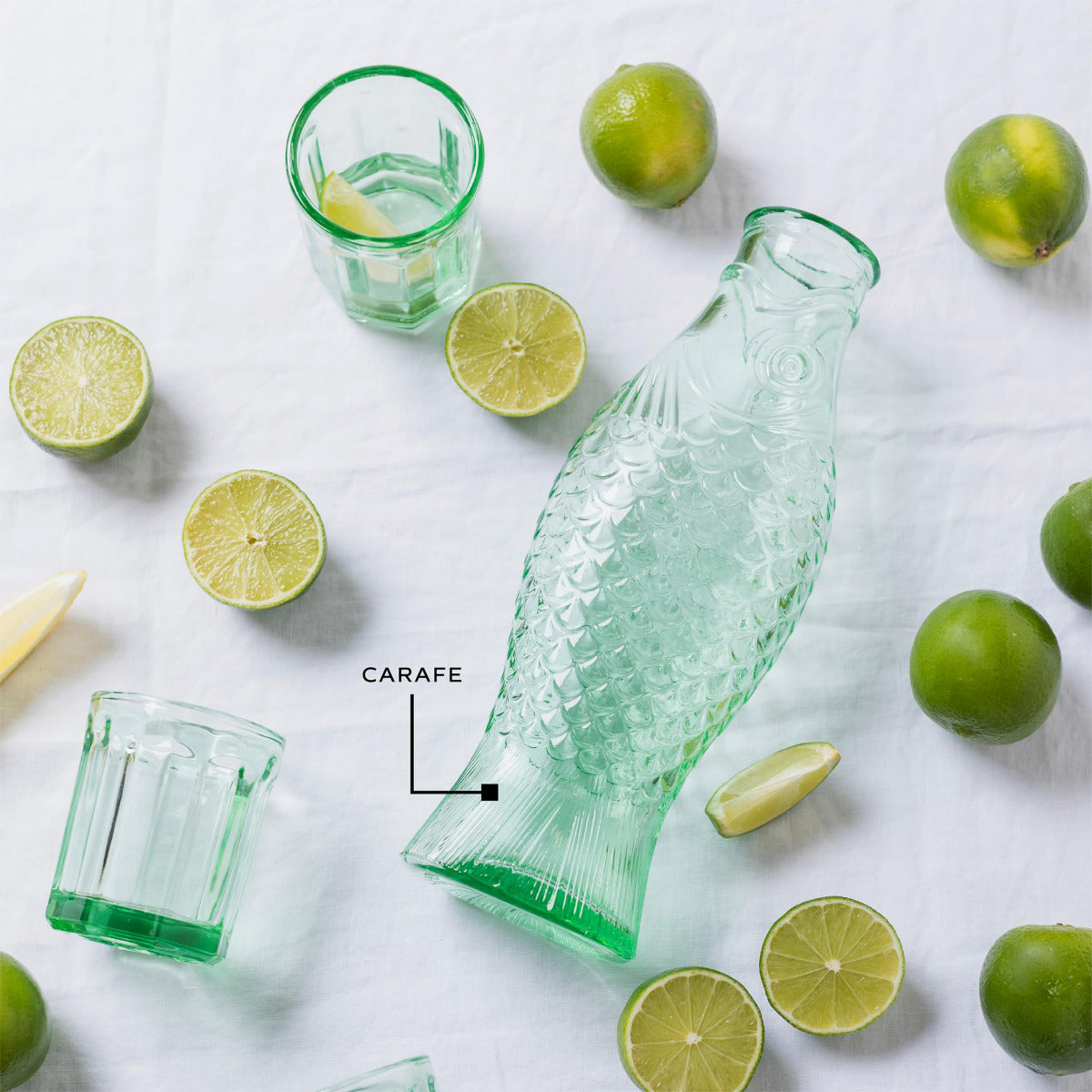 Green glass carafe and glasses with limes on a white background