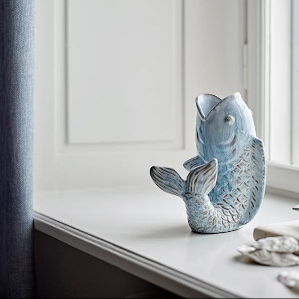 Blue ceramic fish sculpture on a windowsill with a neutral background