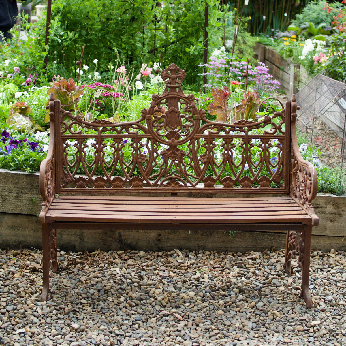 Ornate Shelly garden bench with decorative detailing displayed amongst lush flowering plants at Brookfield Gardens Brisbane.