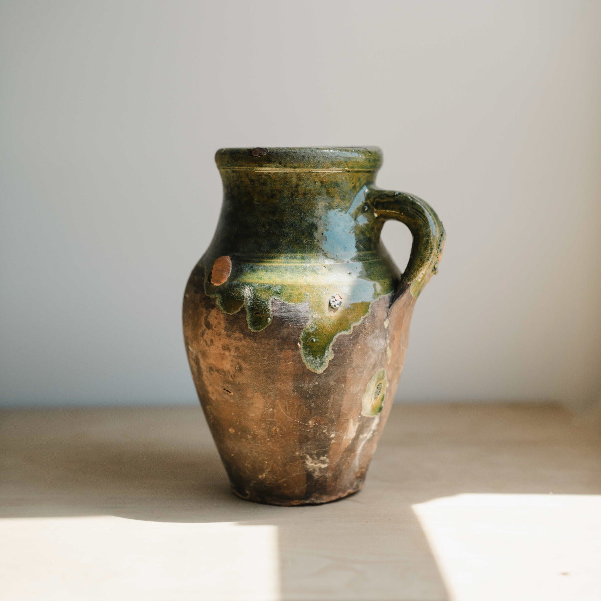Small Turkish green glazed terracotta jugs with aged patina displayed on a timber table.