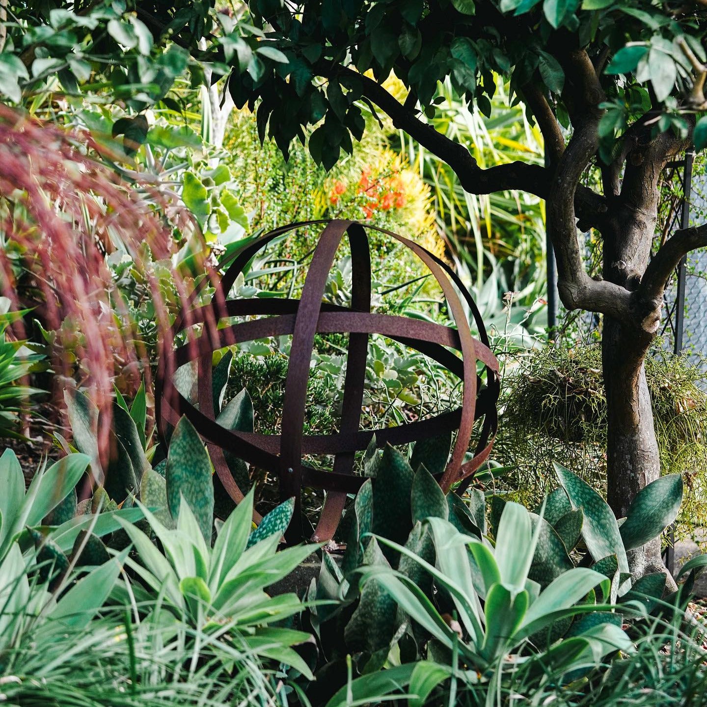 Large rusted steel Strappy Ball garden sculpture with open architectural design, available in 75cm and 100cm sizes.