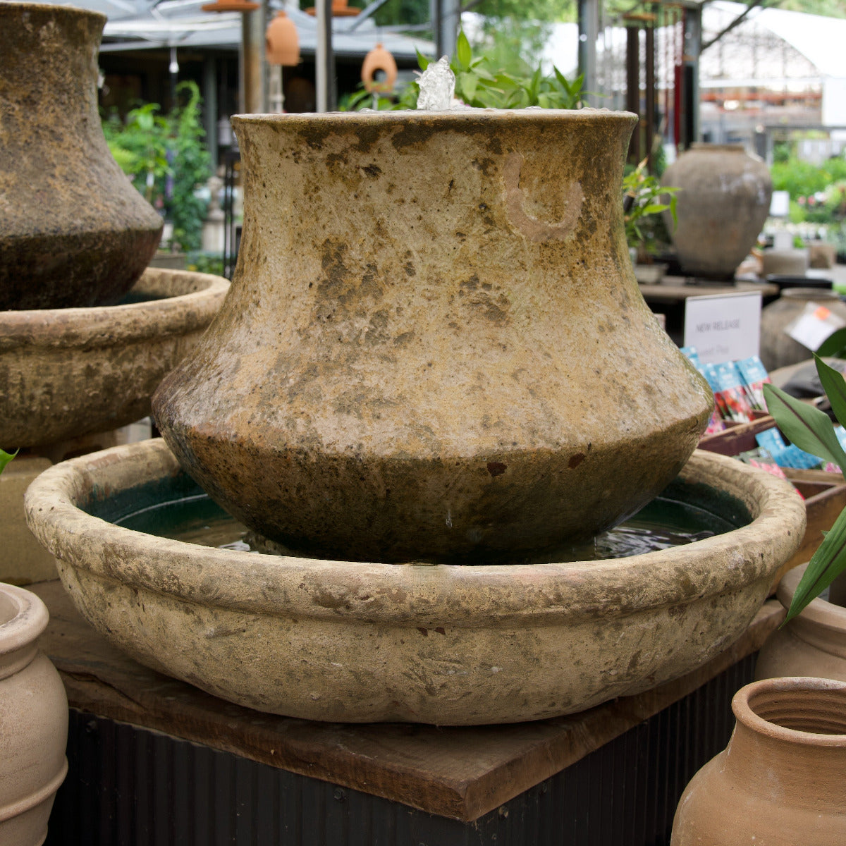 Decorative stone water feature with a bowl and vase-like structure in a garden setting.