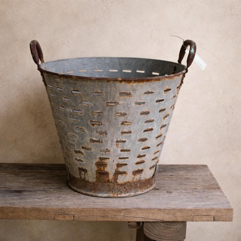 Aged galvanised perforated metal harvest basket with rusted handles and industrial patina.