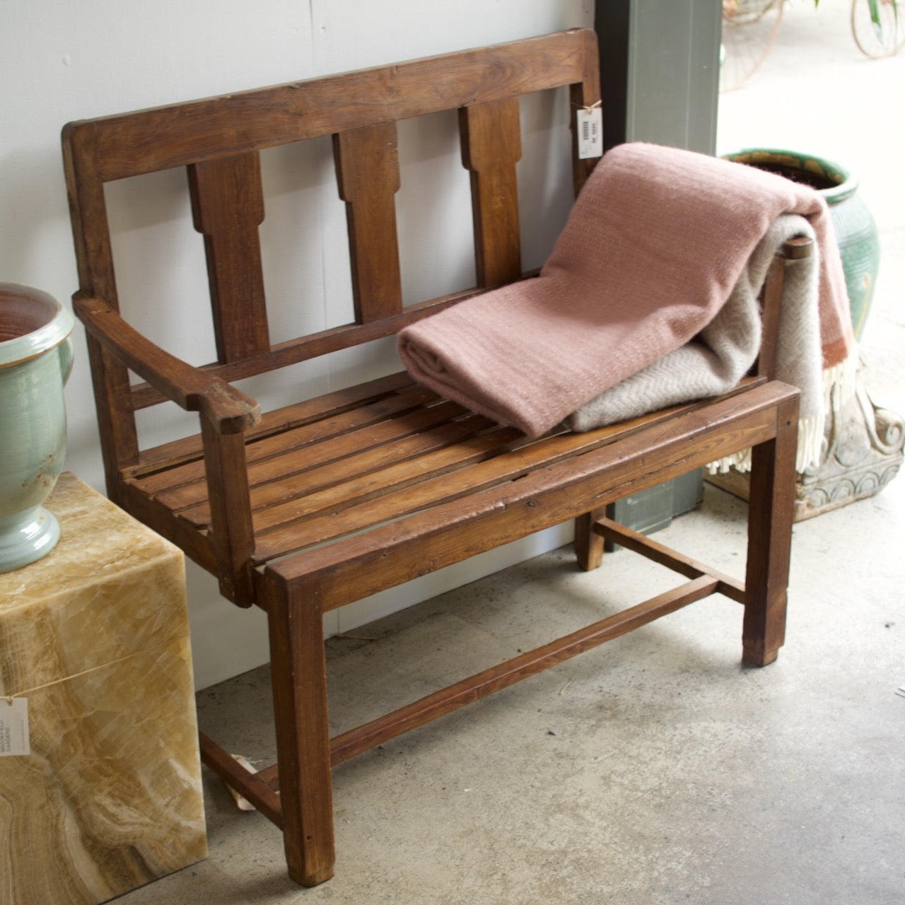 Quant wooden bench with slatted seat and natural finish, styled with a soft throw in a garden setting.