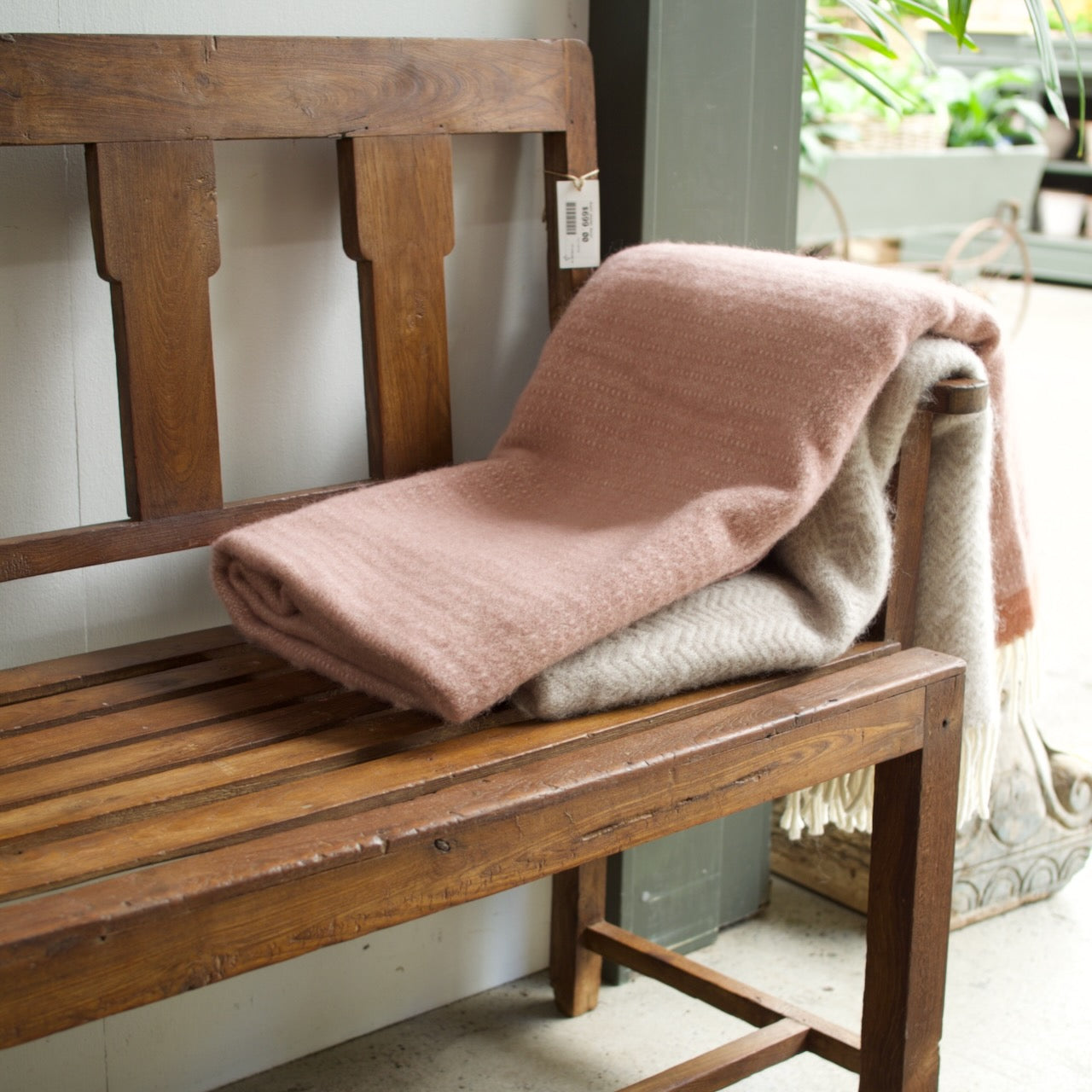 A dusty pink and beige textured throw blanket is draped over a rustic wooden bench in a home-like setting.