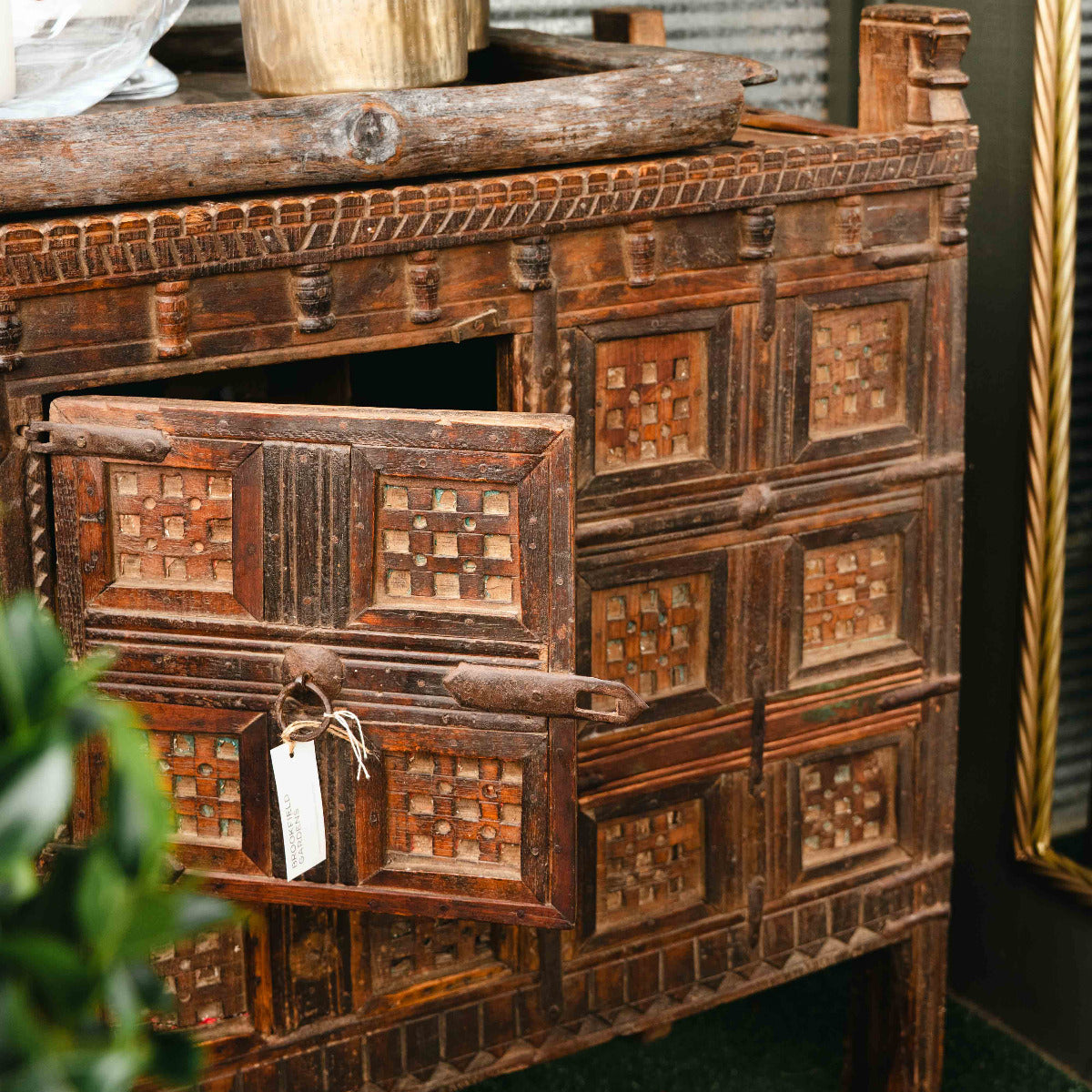 Vintage wooden cabinet with intricate carvings and a plant on top, set against a neutral wall.