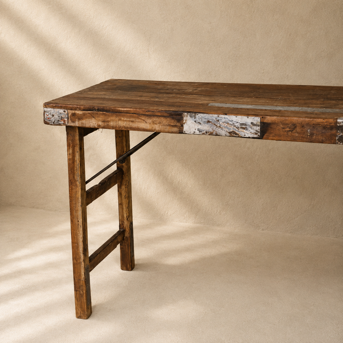 A rustic wooden console table with a dark brown wood top, distressed metal accents, and a ladder-style support leg, photographed against a textured beige backdrop.