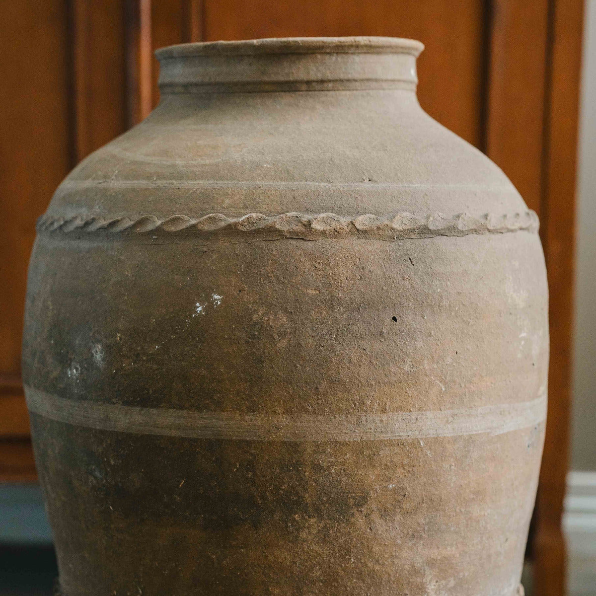 Large brown ceramic vase with decorative patterns on a neutral background