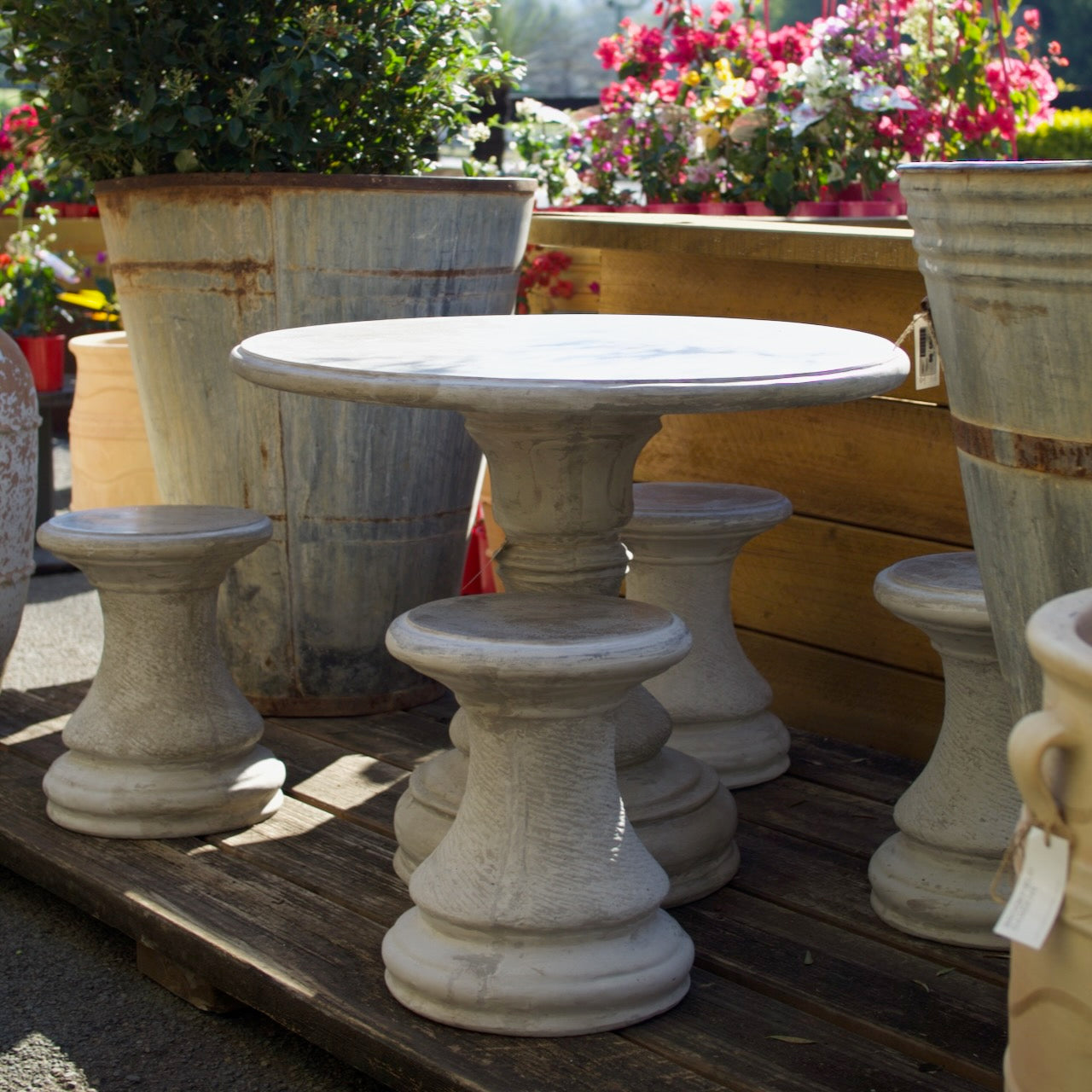 French-inspired round concrete outdoor table with four matching stools in a garden setting. Exclusive to Brookfield Gardens.