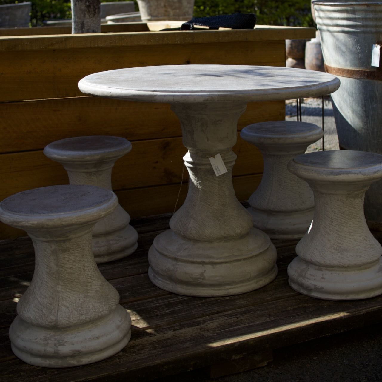 A set of outdoor garden furniture featuring a round stone-look table and four matching pedestal stools, displayed on a wooden pallet in an outdoor setting.