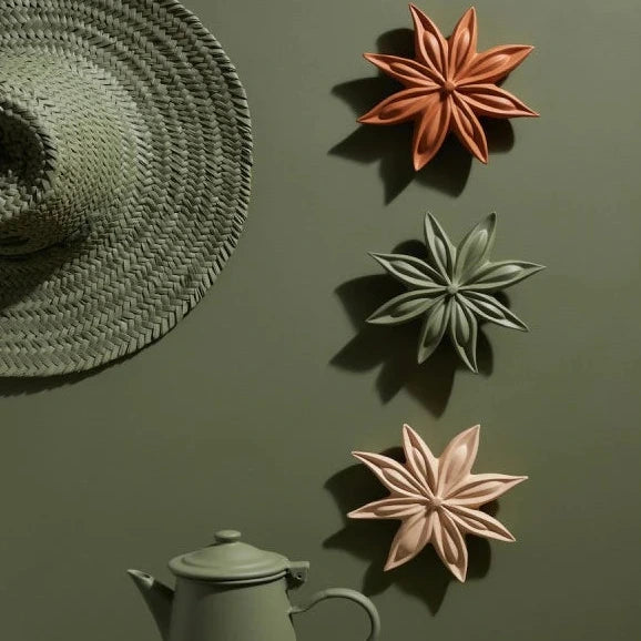Decorative star-shaped objects on a green wall with a teapot below.