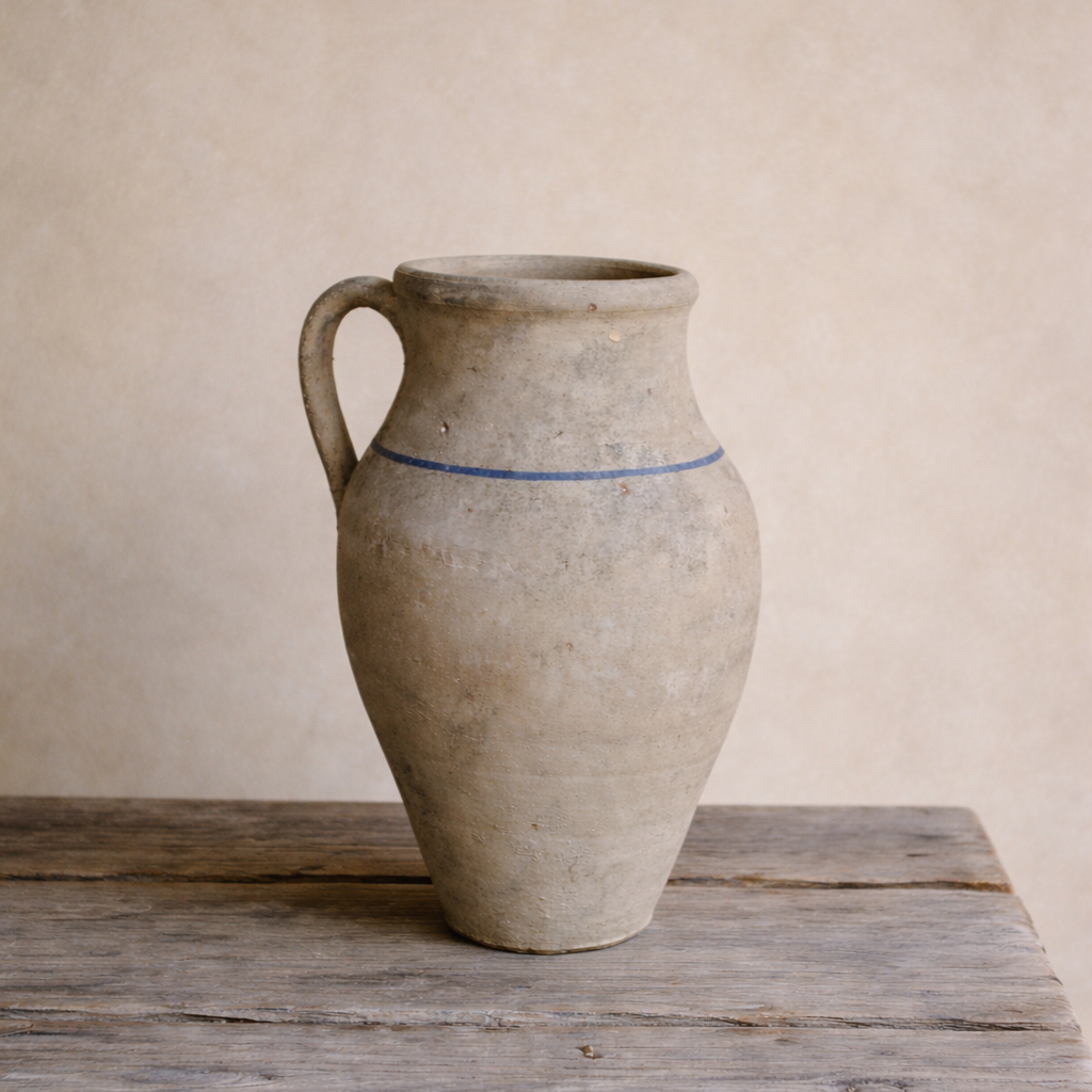 Handcrafted Turkish terracotta urn with single handle and faded blue stripe, styled on a rustic table.
