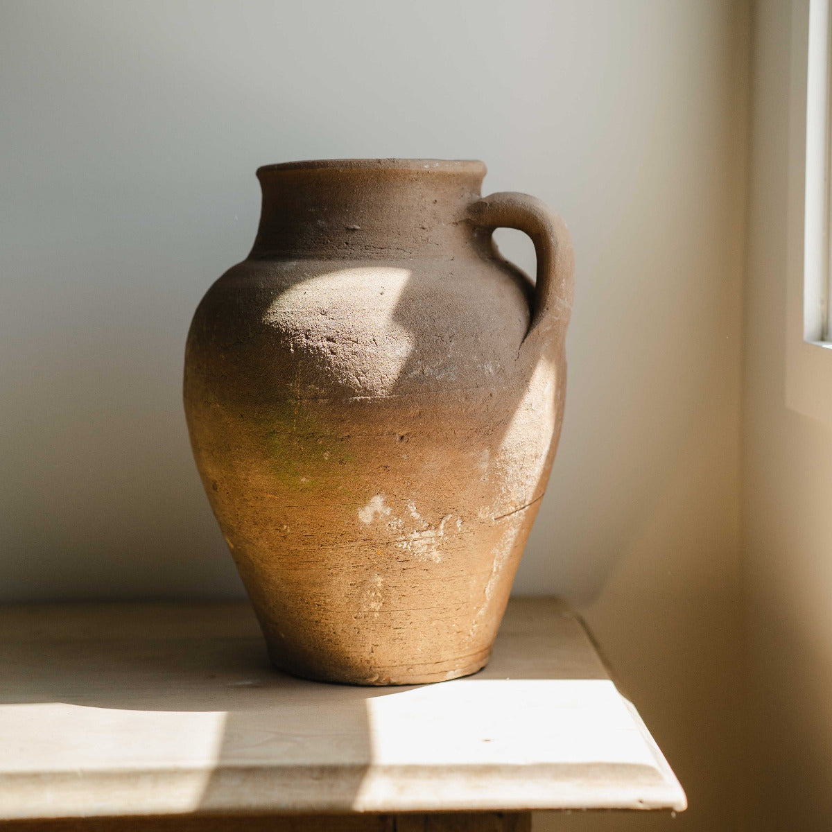 Aged Turkish terracotta pot with single handle styled indoors in natural light.