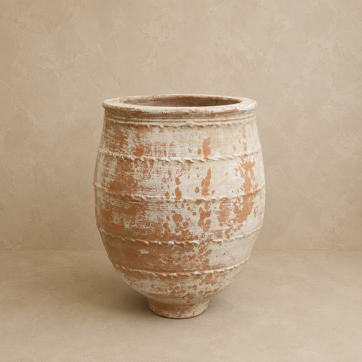 A large rustic ceramic planter pot with a distressed, weathered finish showing terracotta brown underneath a cream and off-white glaze, set against a neutral textured beige background.