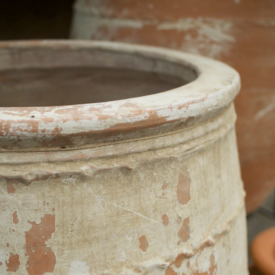 Close-up of a large rustic terracotta clay pot with a weathered, peeling white and beige stucco-like finish showing the warm orange-brown clay underneath.