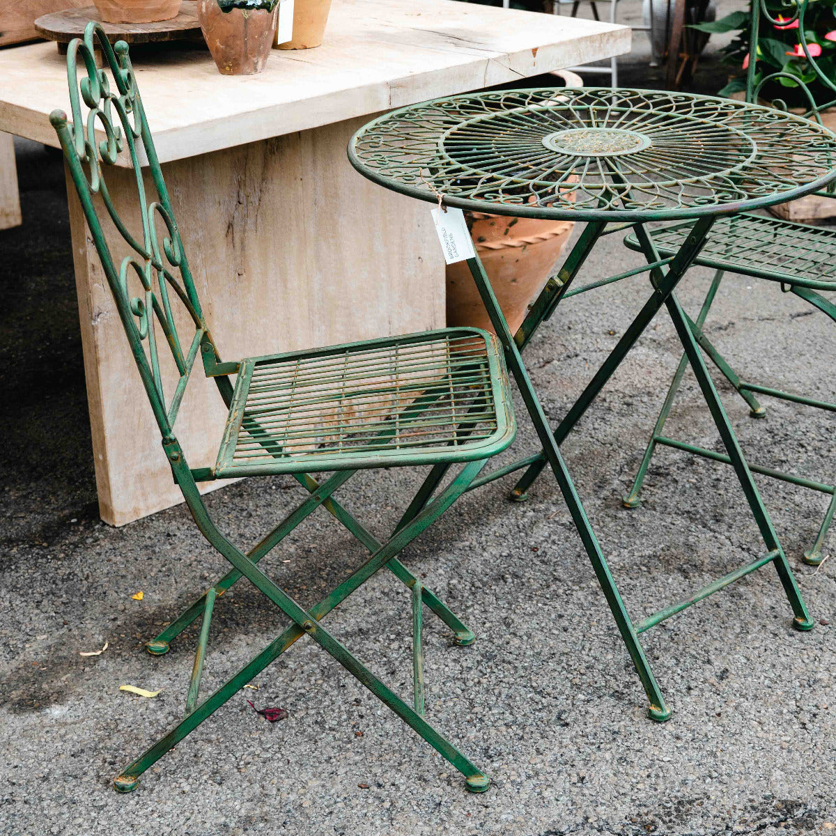 Green metal chair and table set on a patio with potted plants in the background