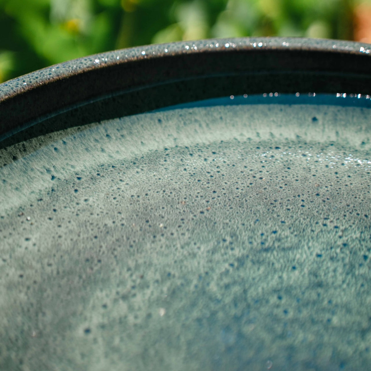 Wren Bird Bath in Almond glaze with rounded bowl and pedestal base in a lush garden setting.