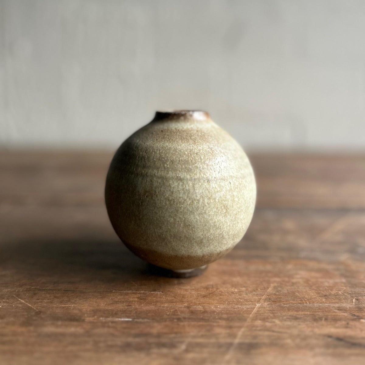 Small ceramic vase on a wooden surface with a neutral background