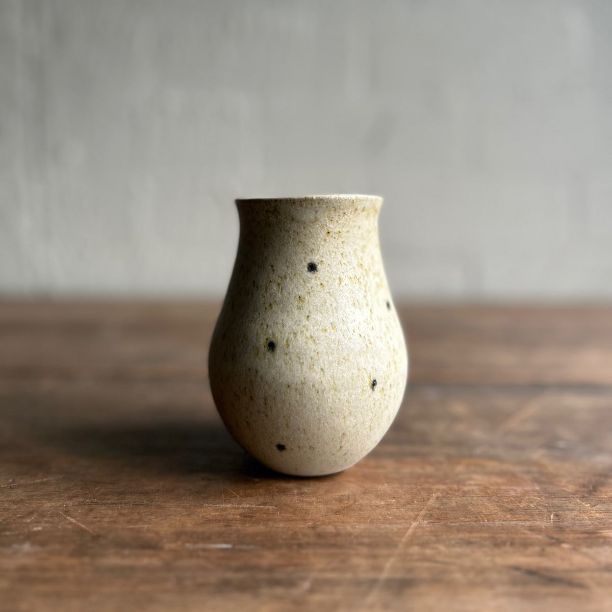 Speckled ceramic vase on a wooden surface with a neutral background
