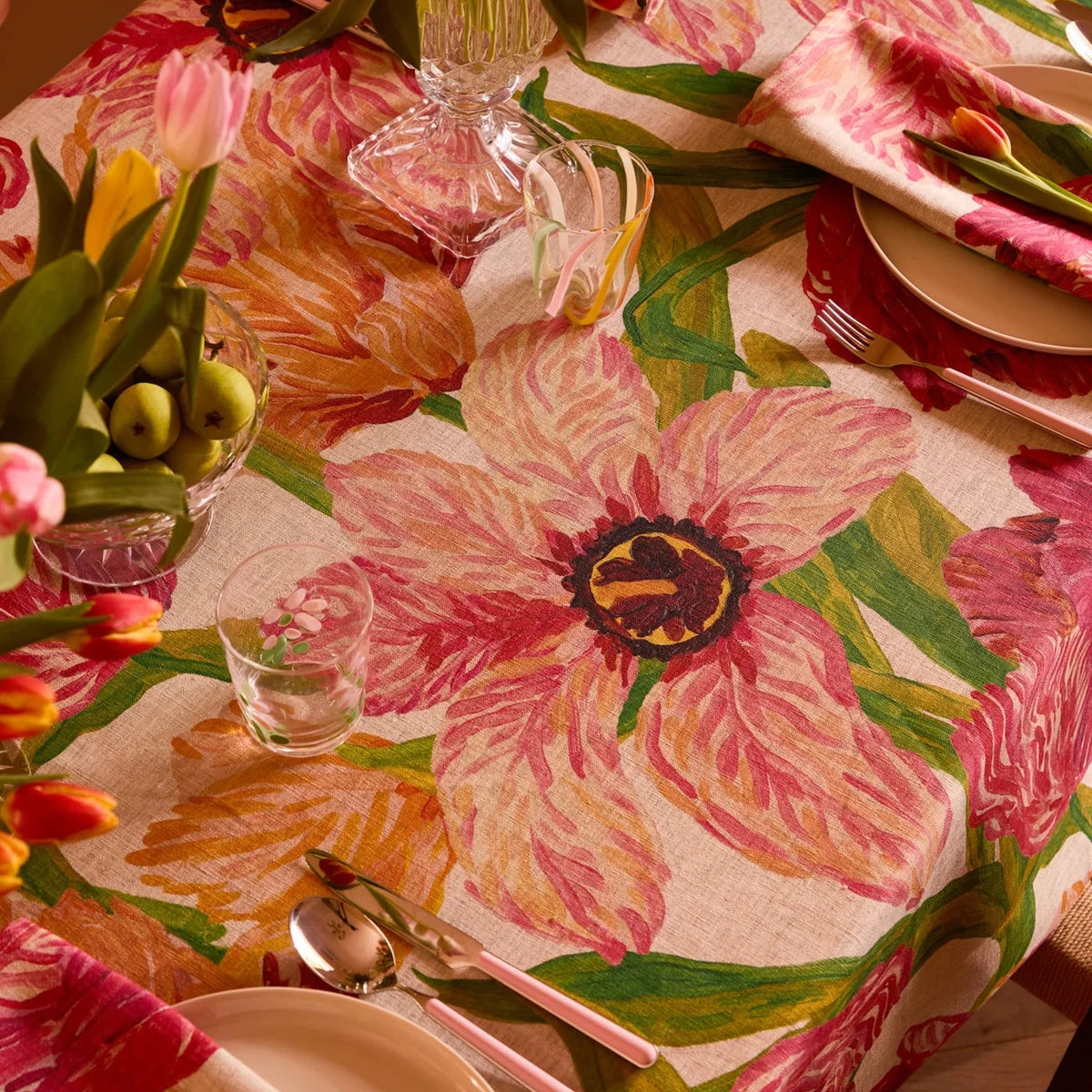 Table setting with a floral tablecloth featuring pink and green flowers.
