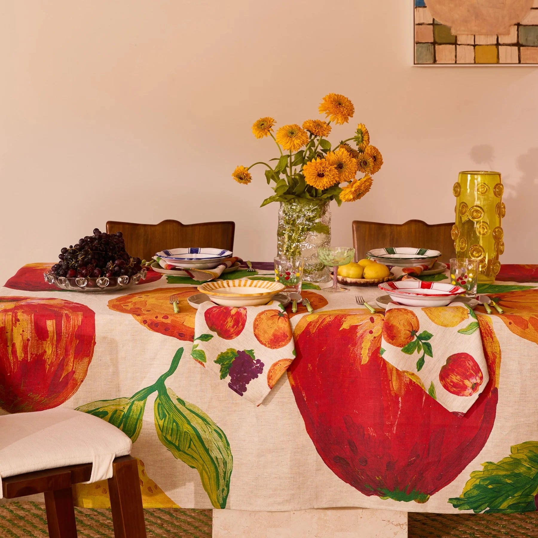 Dining table set with a colorful tablecloth featuring fruit designs, surrounded by chairs.