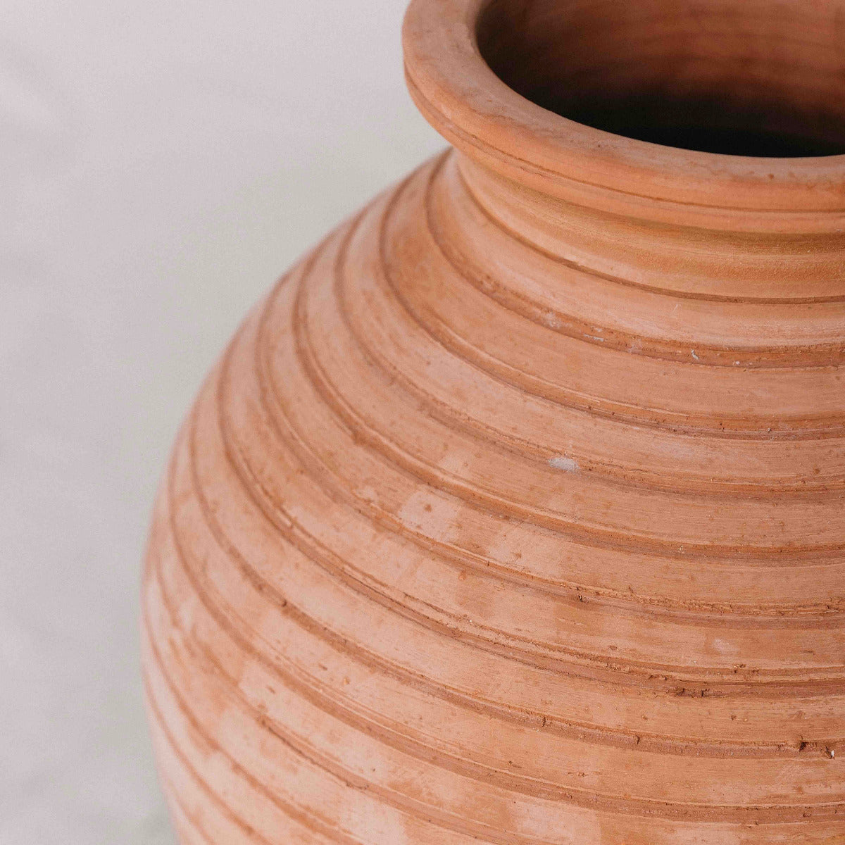 Large terracotta clay urn with rounded form, rolled rim and horizontal textured detailing.