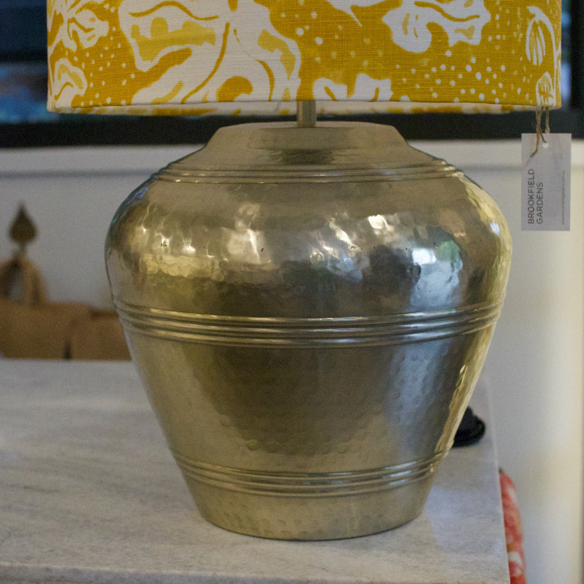 Gold vase on a surface with a patterned lampshade in the background
