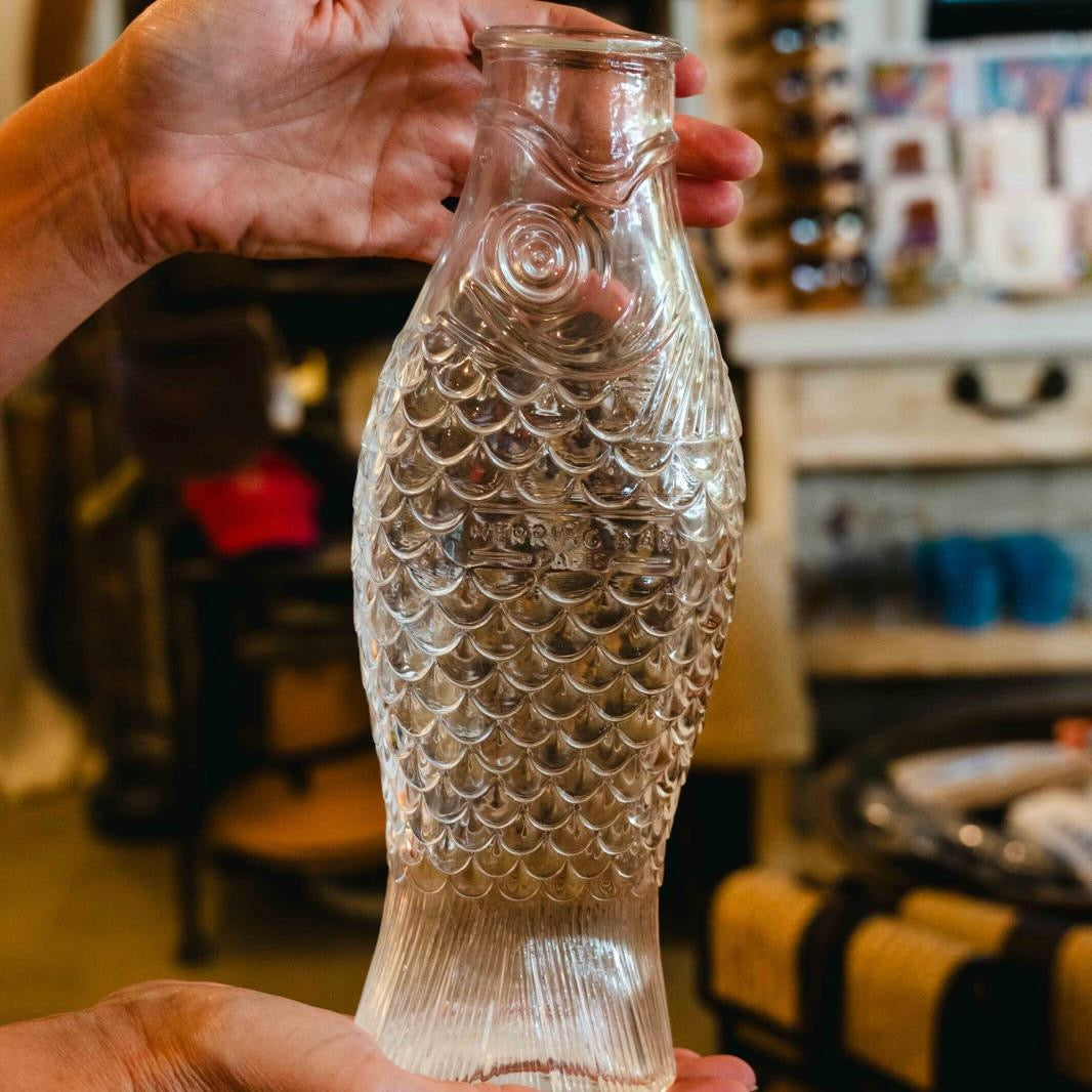Person holding a fish-shaped glass bottle with a blurred indoor background