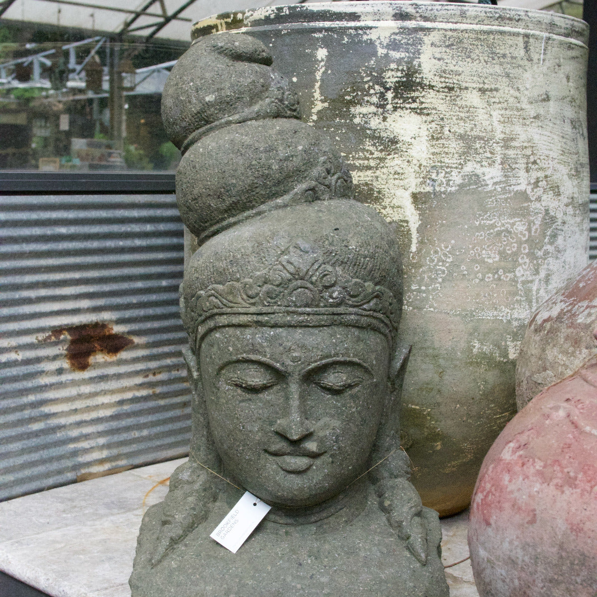 Stone sculpture of a face with intricate details in front of large pots.