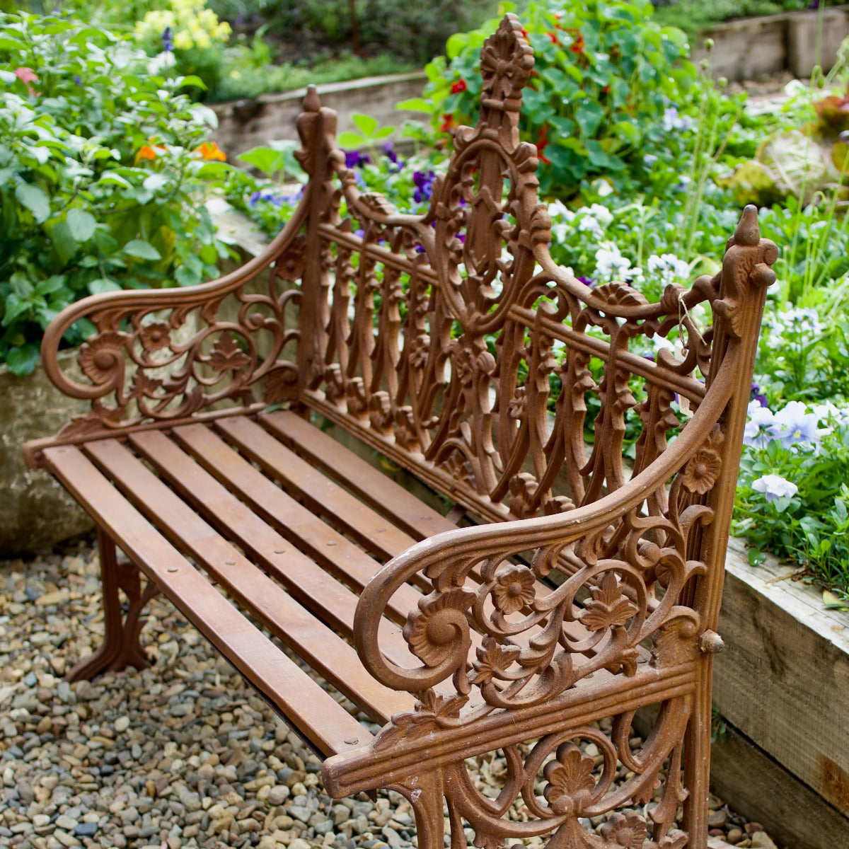 Ornate Shelly garden bench with decorative detailing displayed amongst lush flowering plants at Brookfield Gardens Brisbane.
