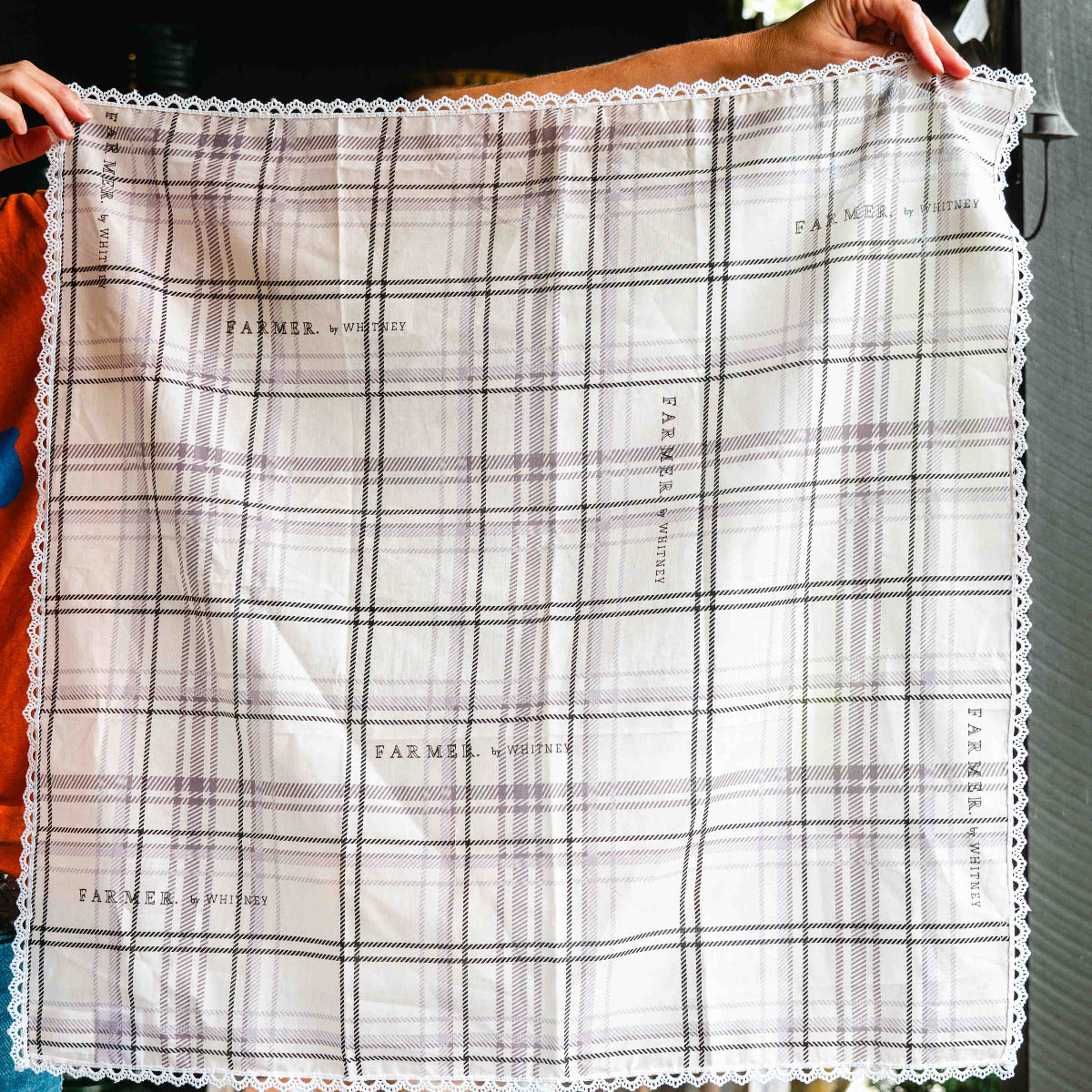 Person holding a plaid fabric swatch with 'Farmers Market' branding.