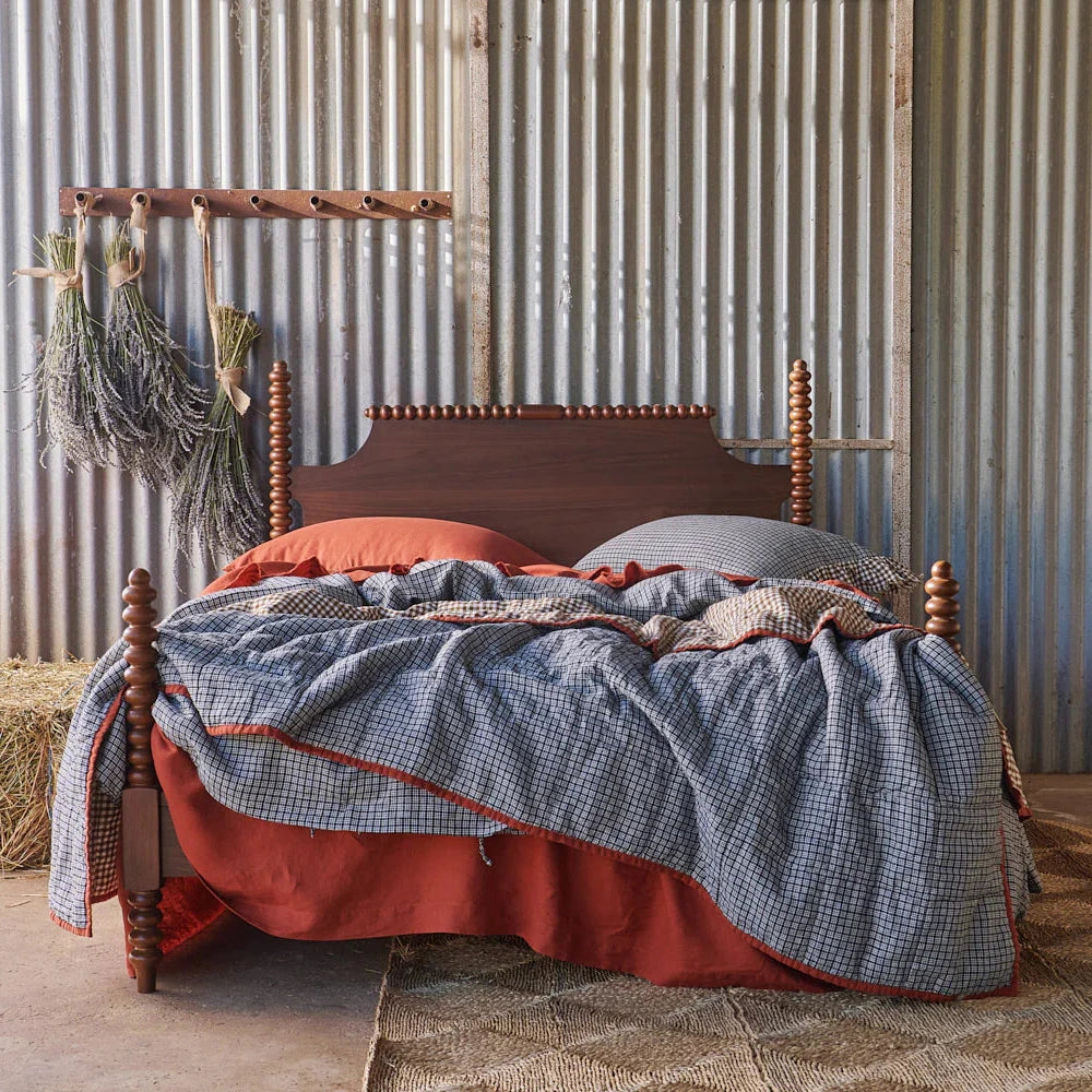 Bed with red and blue bedding against a corrugated metal wall.