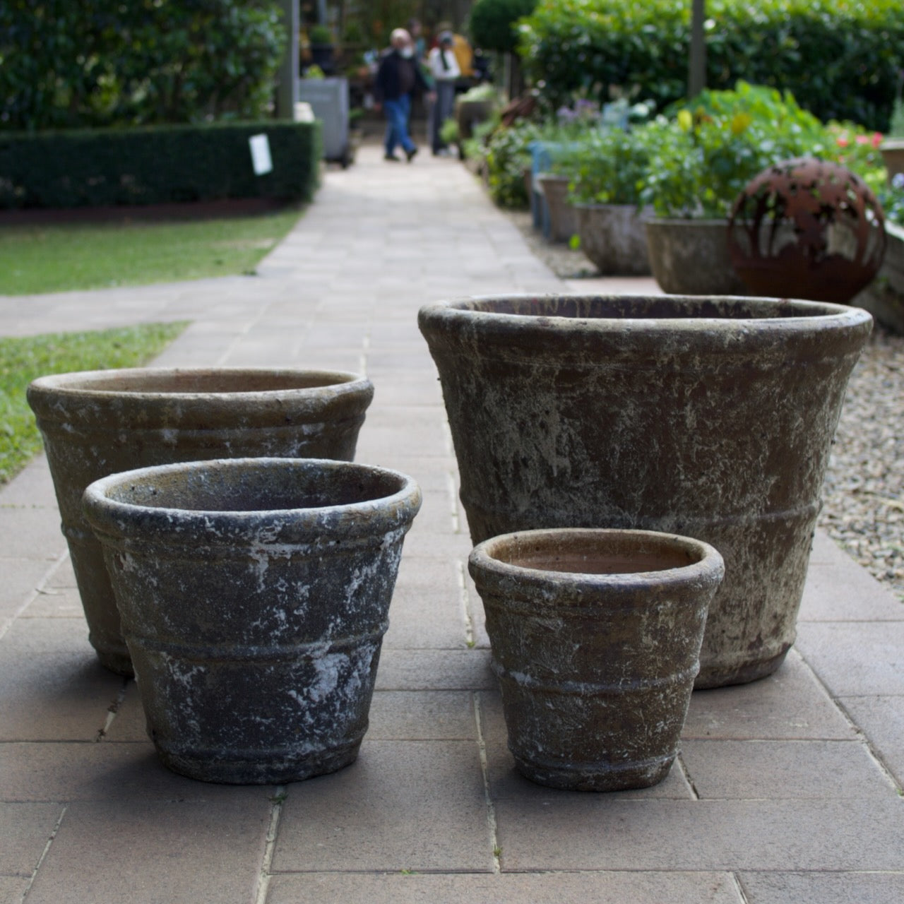 Four weathered terracotta planter pots in different sizes arranged on a stone pathway in a garden setting.