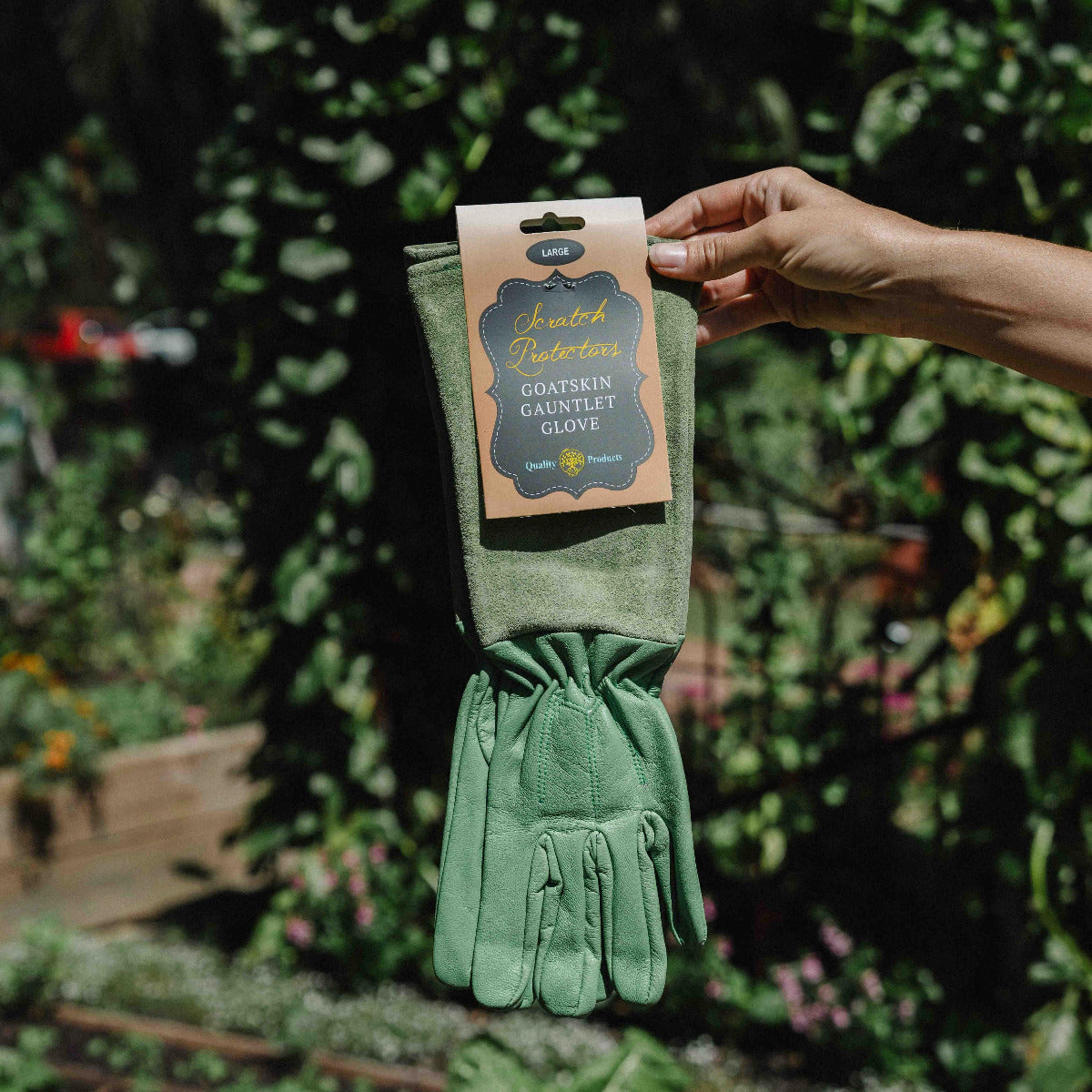Green gardening gloves in packaging held by a hand with a garden background