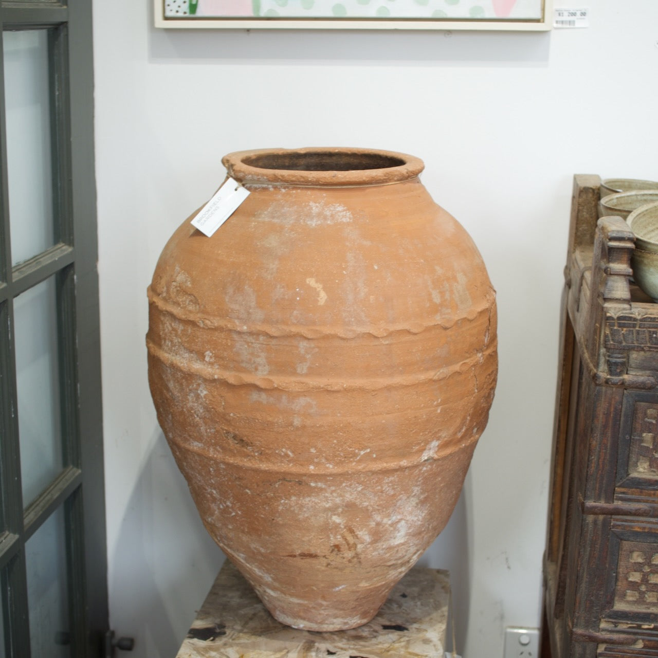 Terracotta pot with a tag on a wooden surface with other pots and plants in the background.