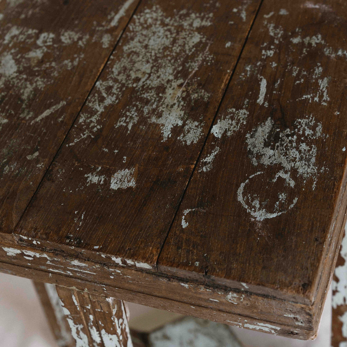 Close-up of a rustic wooden table with a dark brown finish and heavily distressed, peeling white paint showing the wood grain underneath.
