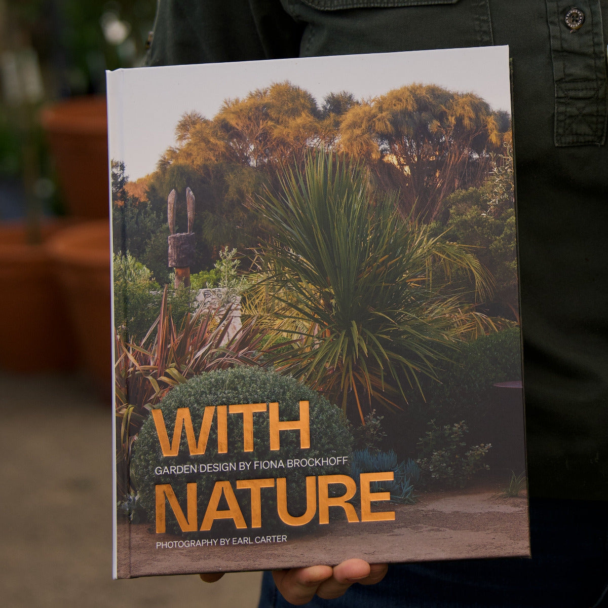 Book titled 'With Nature' held by a person, with garden design and photography credits.