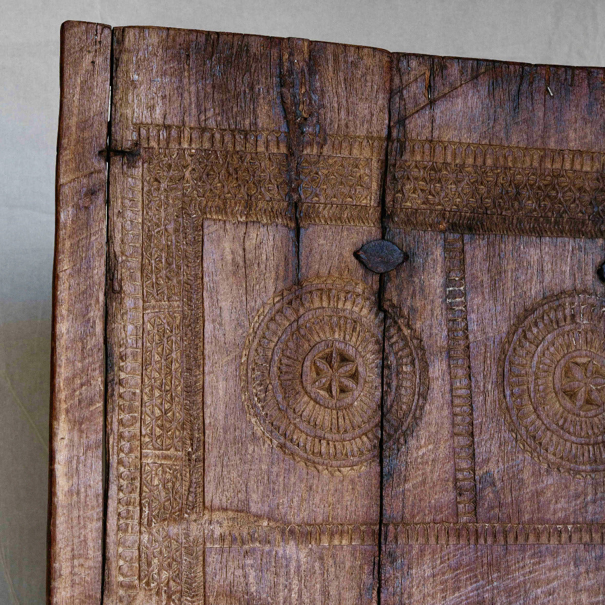 Close-up of a carved wooden panel with intricate geometric and circular patterns, showing natural wood grain and texture.