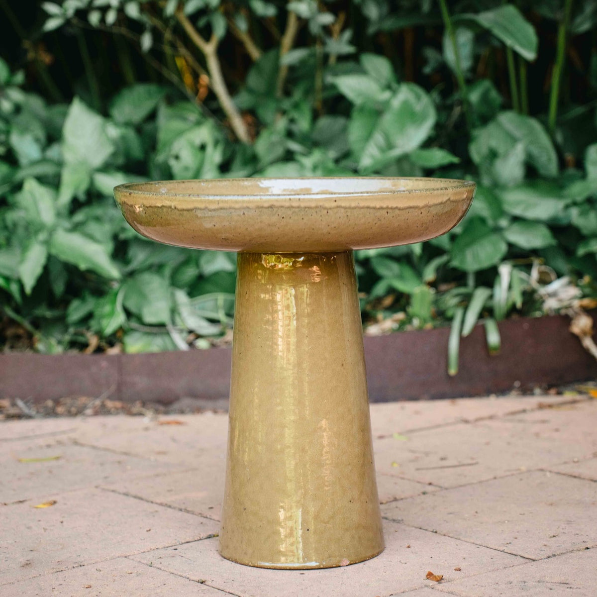 Wren Bird Bath in Almond glaze with rounded bowl and pedestal base in a lush garden setting.