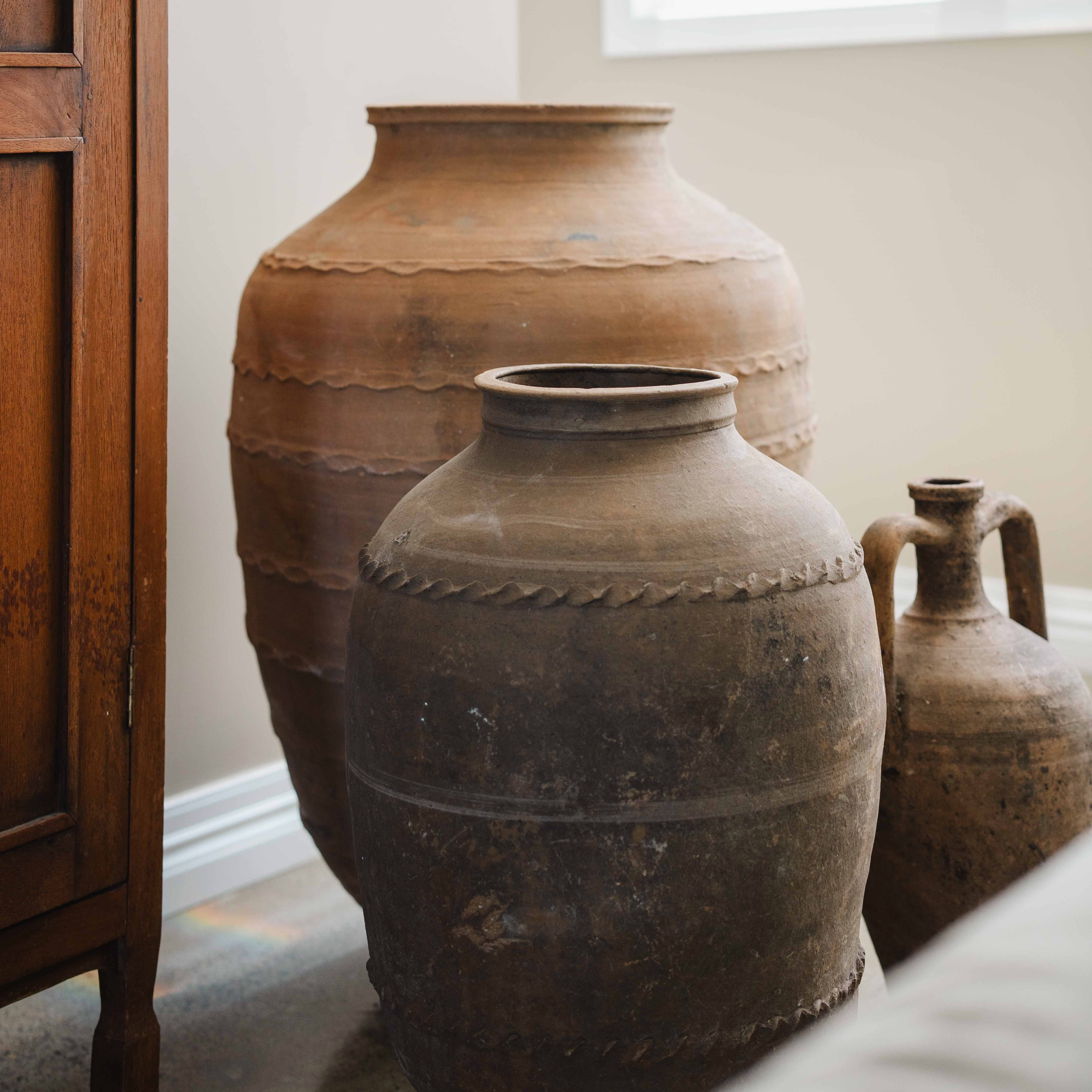 Three large brown ceramic pots on a surface with a wooden cabinet in the background.