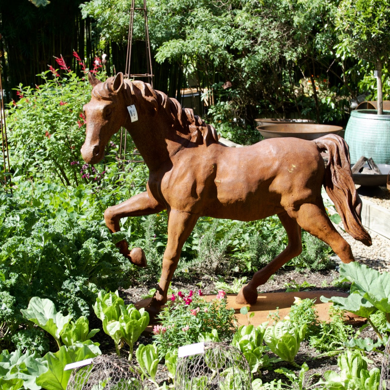 Large cast iron horse garden statue with natural rust patina displayed amongst lush vegetable and cottage garden planting.