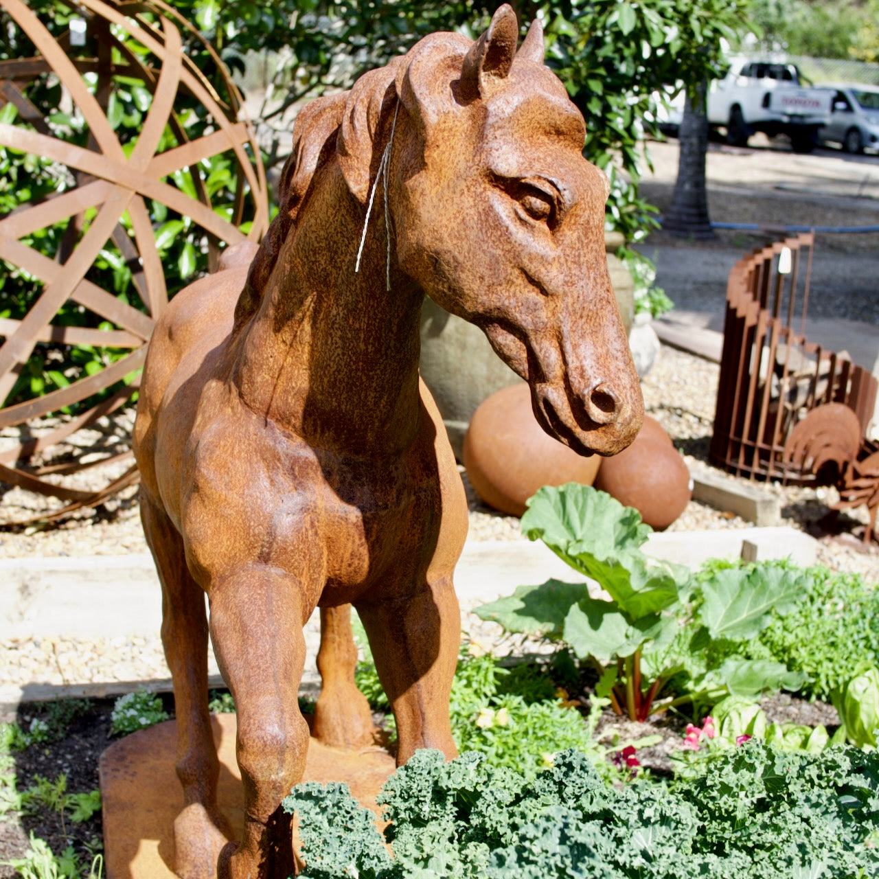 Large cast iron horse garden statue with natural rust patina displayed amongst lush vegetable and cottage garden planting.
