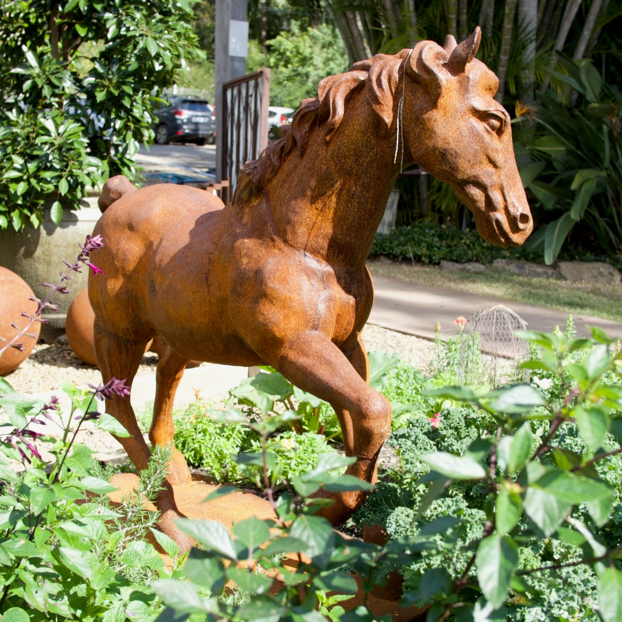 Large cast iron horse garden statue with natural rust patina displayed amongst lush vegetable and cottage garden planting.